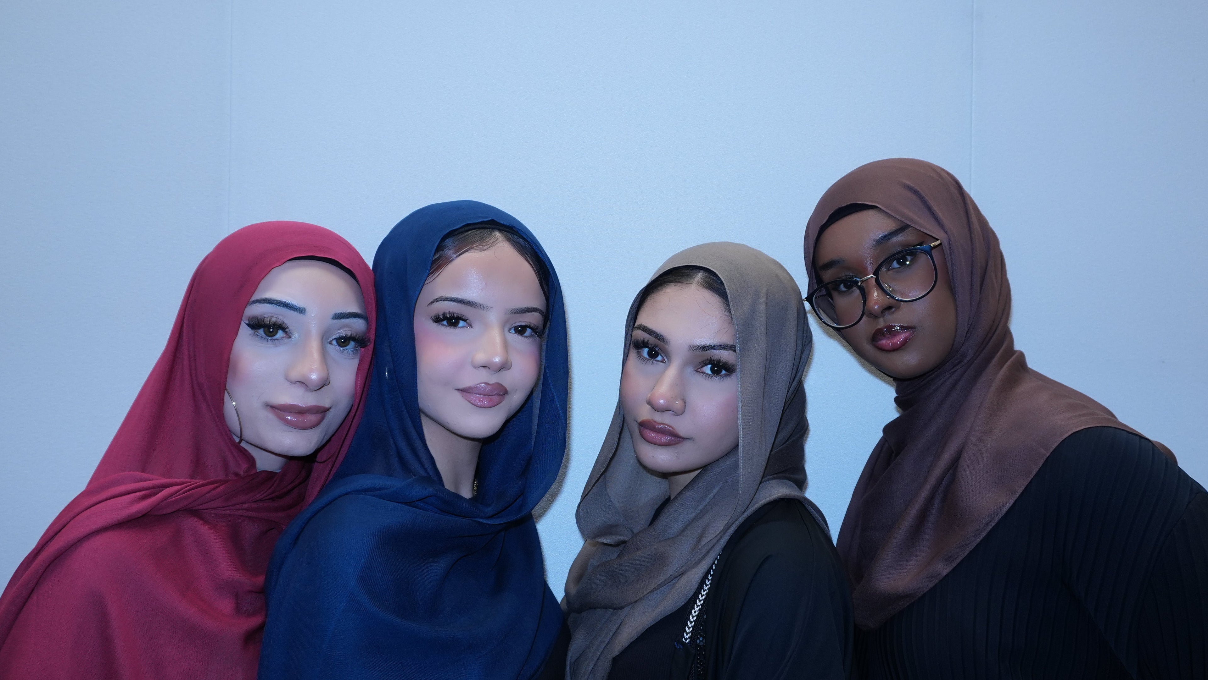 Four women wearing hijabs posing together against a plain background